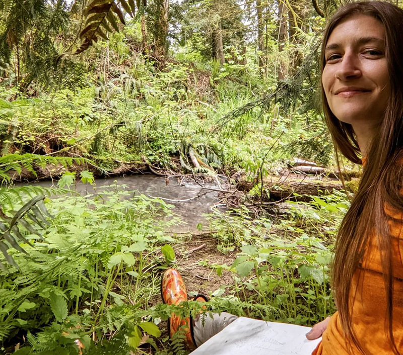 An artist sitting on the banks of a green stream